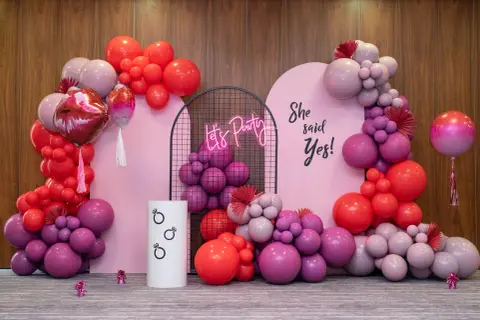 Girlanda z różowych i czerwonych balonów, neonowy napis "Let's Party" i napis "She said Yes!".