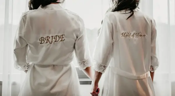 Dwie kobiety w szatach, jedna z napisem "BRIDE", druga "Maid of Honor". Idealny obrazek, by zainspirować się, jak poprosić świadka na ślub.