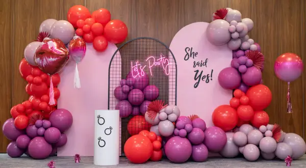Girlanda z różowych i czerwonych balonów, neonowy napis "Let's Party" i napis "She said Yes!".