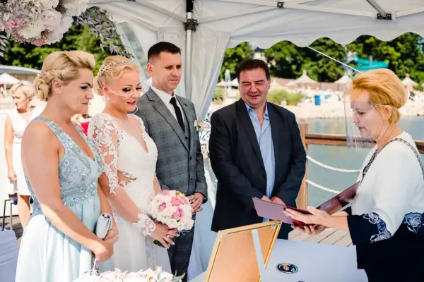 Ślub cywilny nad jeziorem: para młoda, świadkowie i urzędniczka w przyłbicy.